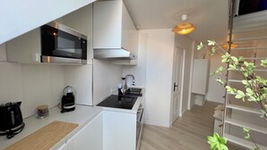 Une cuisine compacte avec des meubles blancs, une cuisinière noire et un four à micro-ondes. On y trouve une planche à découper en bois et une machine à café sur le plan de travail.