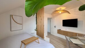 Une chambre d’hôtel moderne, équipée d’un lit, d’une table de chevet, d’une télévision et d’une grande plante.