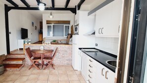 A compact kitchen with a dining area, featuring a brick wall, wooden table, and white cabinetry.