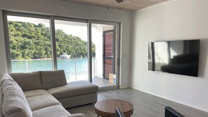 Een moderne woonkamer met een bank, een salontafel, een televisie en uitzicht op water en groen.