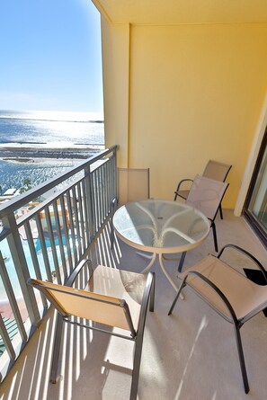 A balcony with a glass table and chairs, overlooking a pool and a beach. - 3-bedroom condo on the 9th floor of EG with superb views of the gulf and harbor. (Destin)