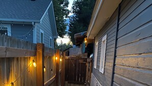 Ein schmaler Weg, begrenzt von Holzzäunen mit Lichterketten, der zu einem Haus mit dunkler Fassade führt.