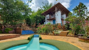 A pool area with a water slide, surrounded by a stone wall and lush greenery. - El Cogollo (Barichara)