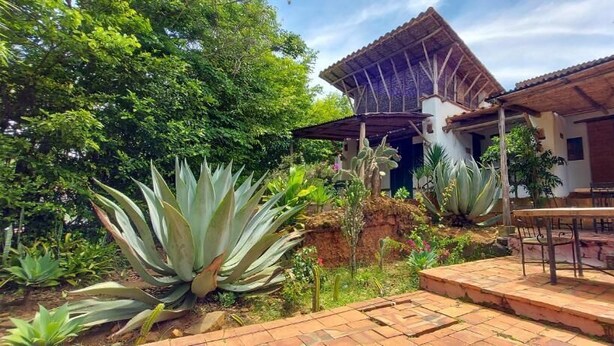 A courtyard with a dining area, a building with a tiled roof, and various plants. - El Cogollo (Barichara)