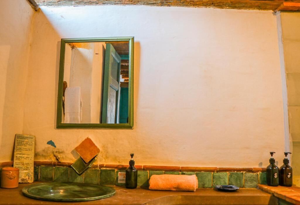 Une salle de bain avec un miroir à cadre vert, une serviette, des distributeurs de savon et un petit récipient.
