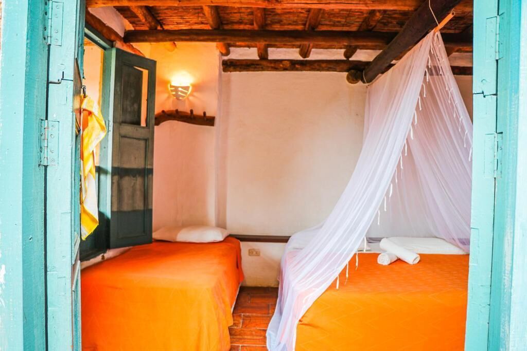 Ein Zimmer mit zwei Betten, jeweils mit einer orangefarbenen Bettdecke, einer Holzzieldecke und einem weißen Baldachinbett.