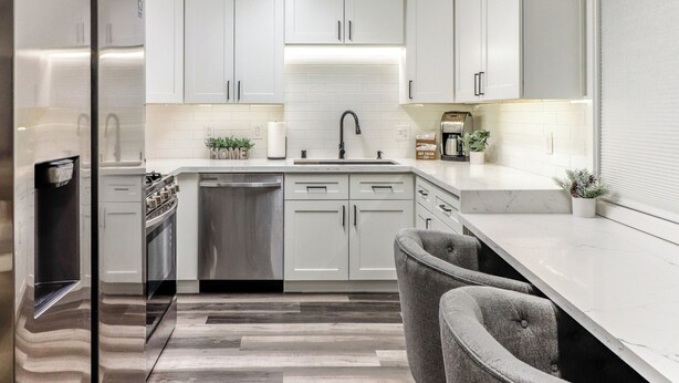A modern kitchen with white cabinets, a stainless steel refrigerator, a dishwasher, and a marble countertop.