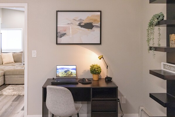 Un espace de bureau moderne comprenant un bureau, une chaise, un ordinateur portable et un tableau abstrait encadré.