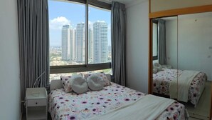 Un dormitorio con un ventanal grande, una cama con ropa de cama floral, una mesita de noche y un espejo.