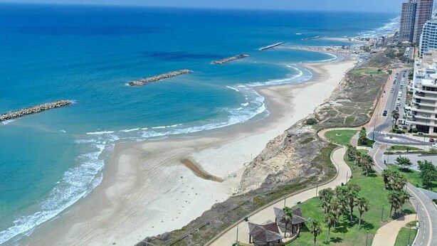 Un paisaje costero con playa, una carretera serpenteando a lo largo de la costa y edificios altos.