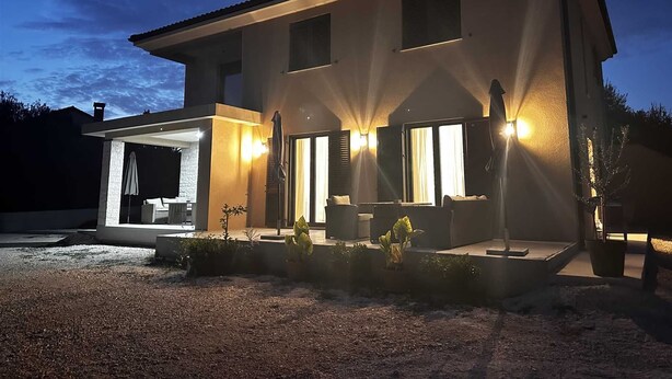 Una casa moderna de dos pisos con un patio cubierto, amplias ventanas e iluminación exterior.