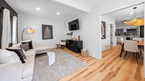 A modern living room with a sofa, a coffee table, and a TV on the wall. There is a dining area with a table and chairs. The room has wooden flooring and white walls. - Charming 2-bedroom house in enchanting Cleveland with AC, WiFi  3219 (Cleveland)