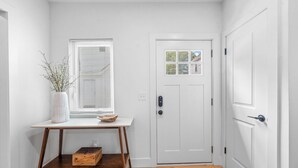 A hallway with a white door, a window with blinds, a small table with a vase and a bowl, and a wooden bench. - Charming 2-bedroom house in enchanting Cleveland with AC, WiFi  3219 (Cleveland)