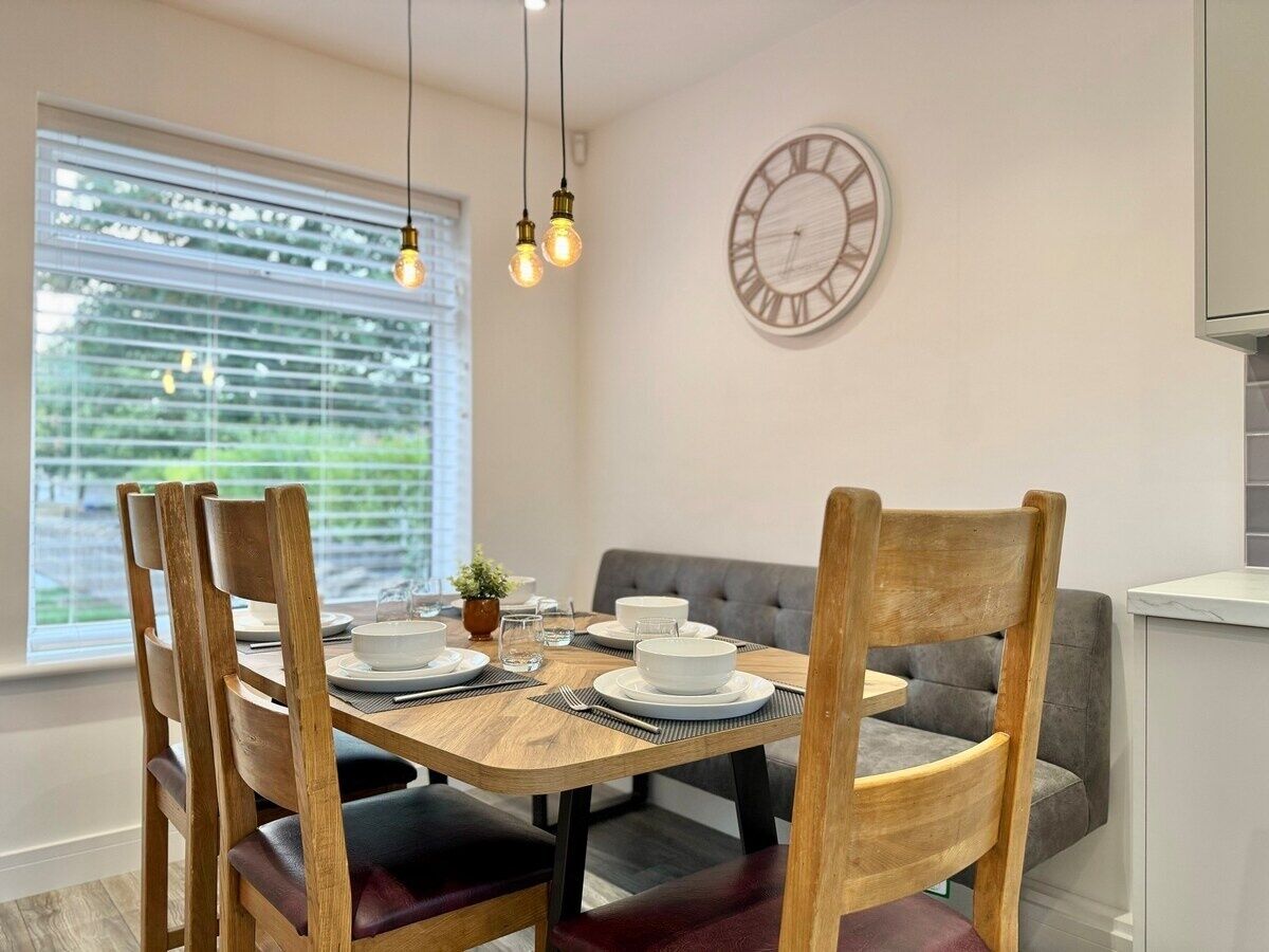 A dining area with a wooden table, four chairs, a grey sofa, and a wall clock.