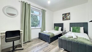 A bedroom with two beds, a desk, a chair, a window with curtains, and a ceiling light.