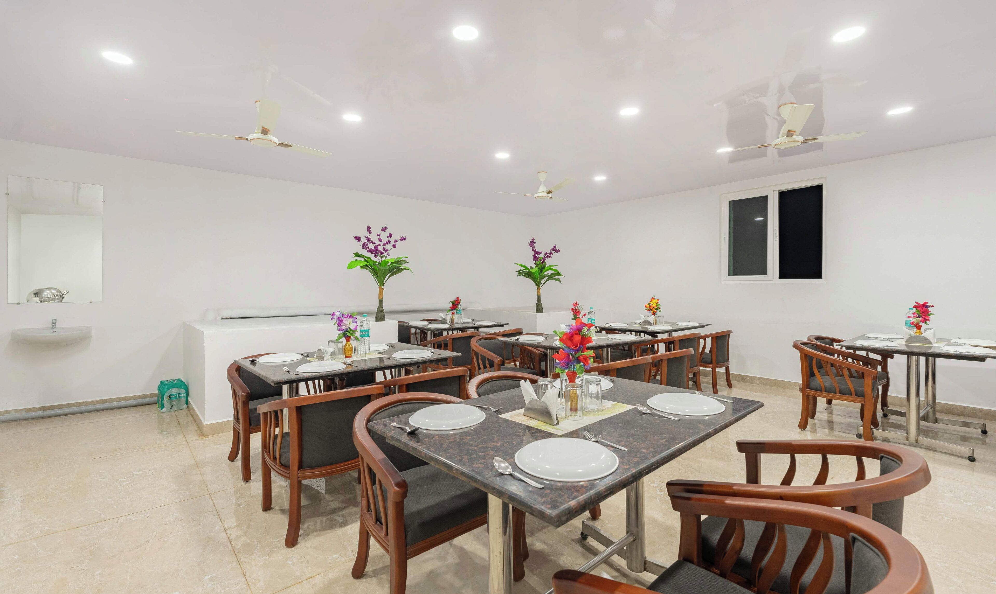 A dining area with multiple tables set for four, each with plates, cutlery, and a vase of flowers.