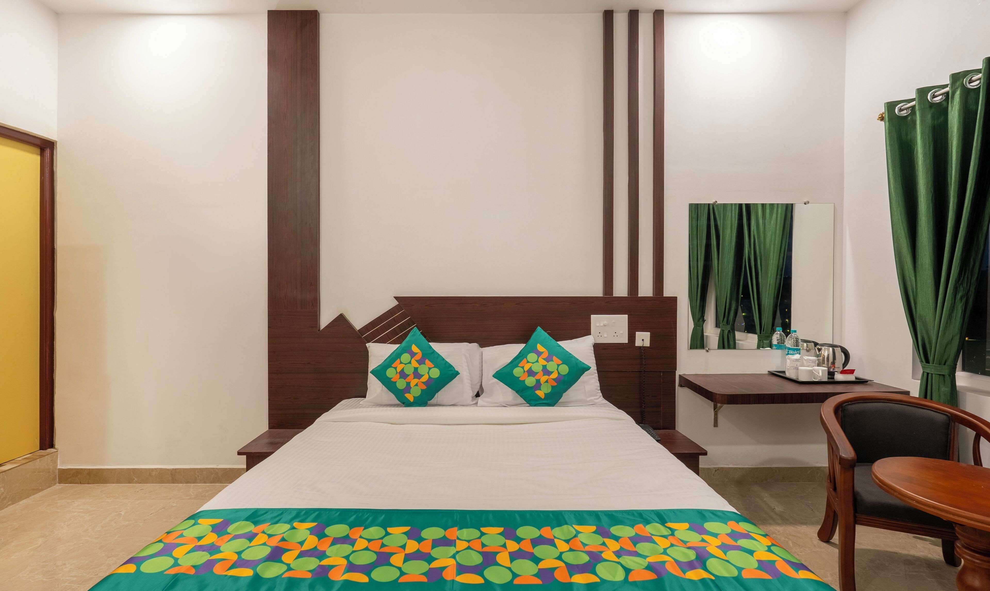 A neatly arranged hotel room with a bed, two pillows, a bedside table with a lamp, a chair, and a window with curtains.