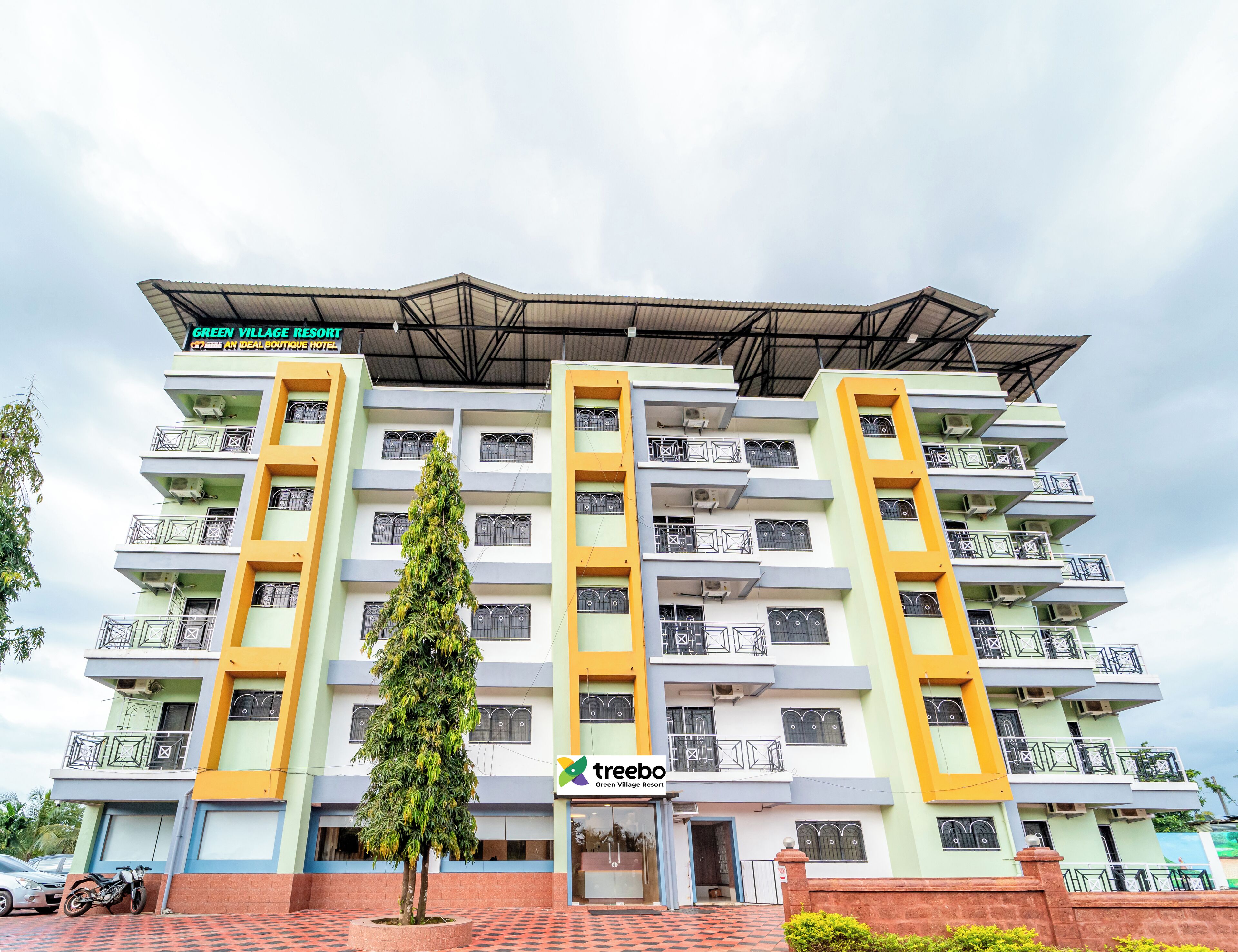 A multi-story hotel with balconies, a central tree, and a sign for 'Green Village Resort Hotel'.