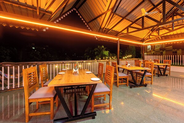 An outdoor dining area with wooden tables and chairs, a glass floor, and a railing. - Treebo Green Village Resort with Pool (Dodamarg)