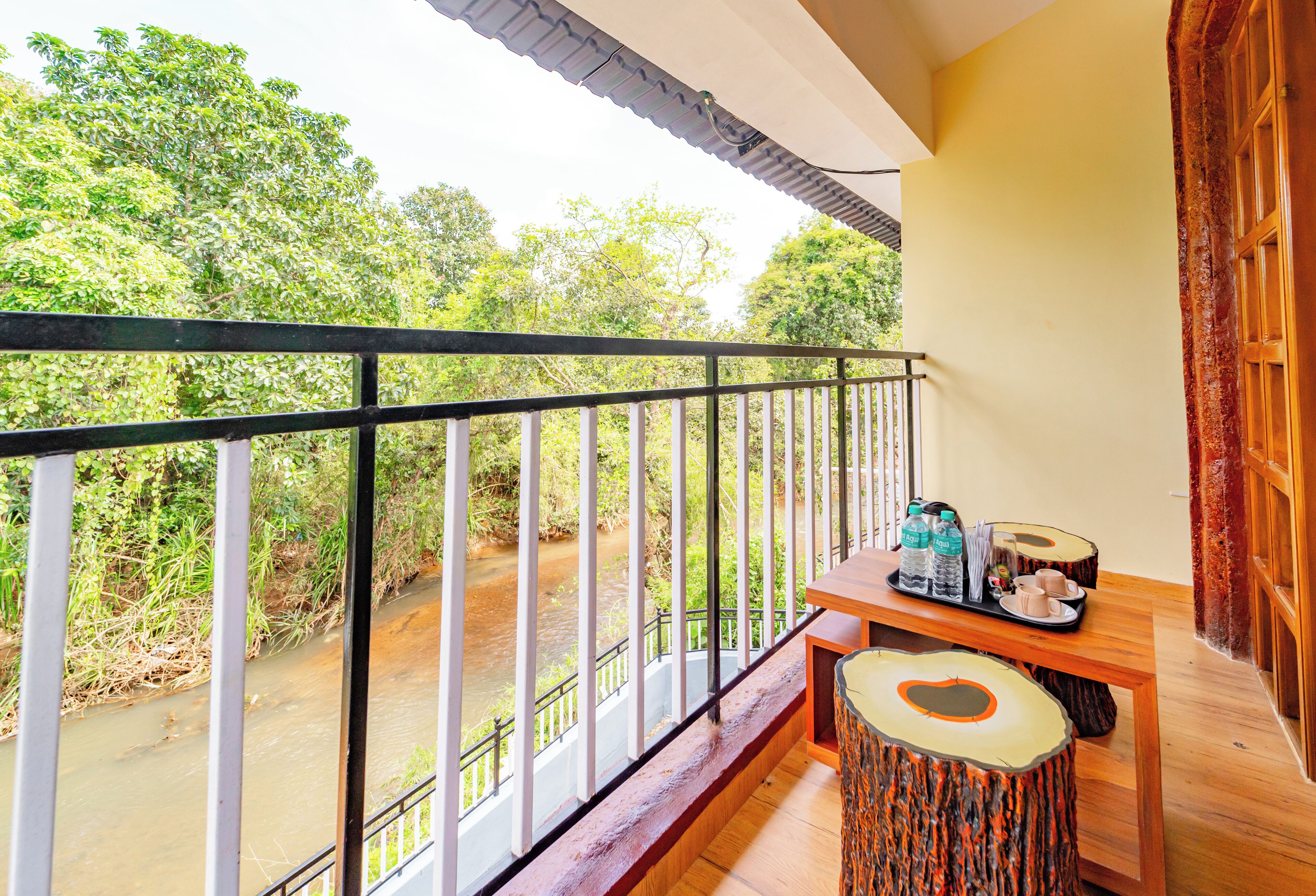 A balcony with a view of a river, a wooden table with a tray of items, and a patterned stool.