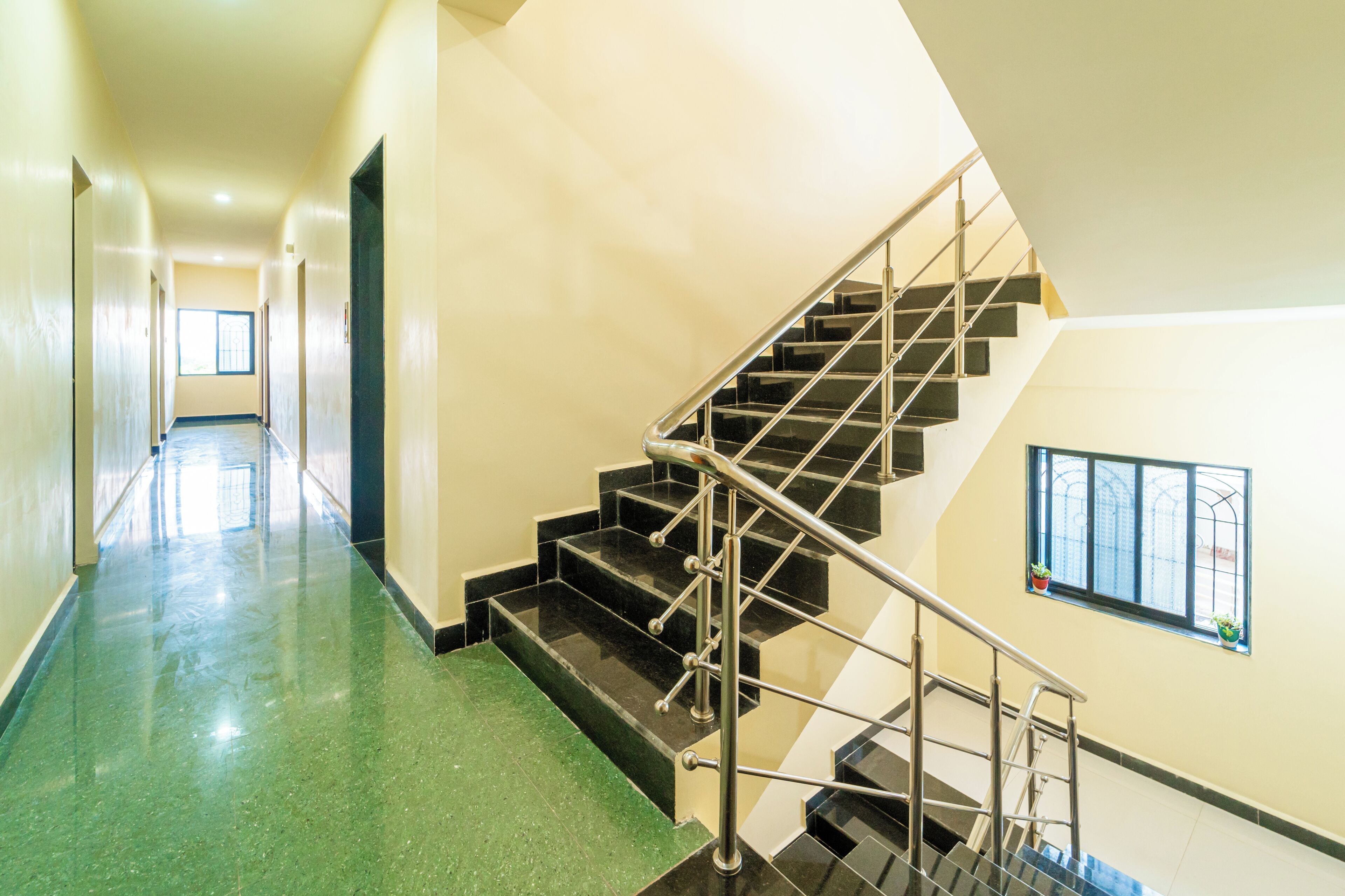 Un pasillo de hotel con una escalera, un ventanal con plantas y una puerta al final.