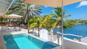 Uma área de piscina com vista clara para o oceano, rodeada por palmeiras e um deque de madeira.