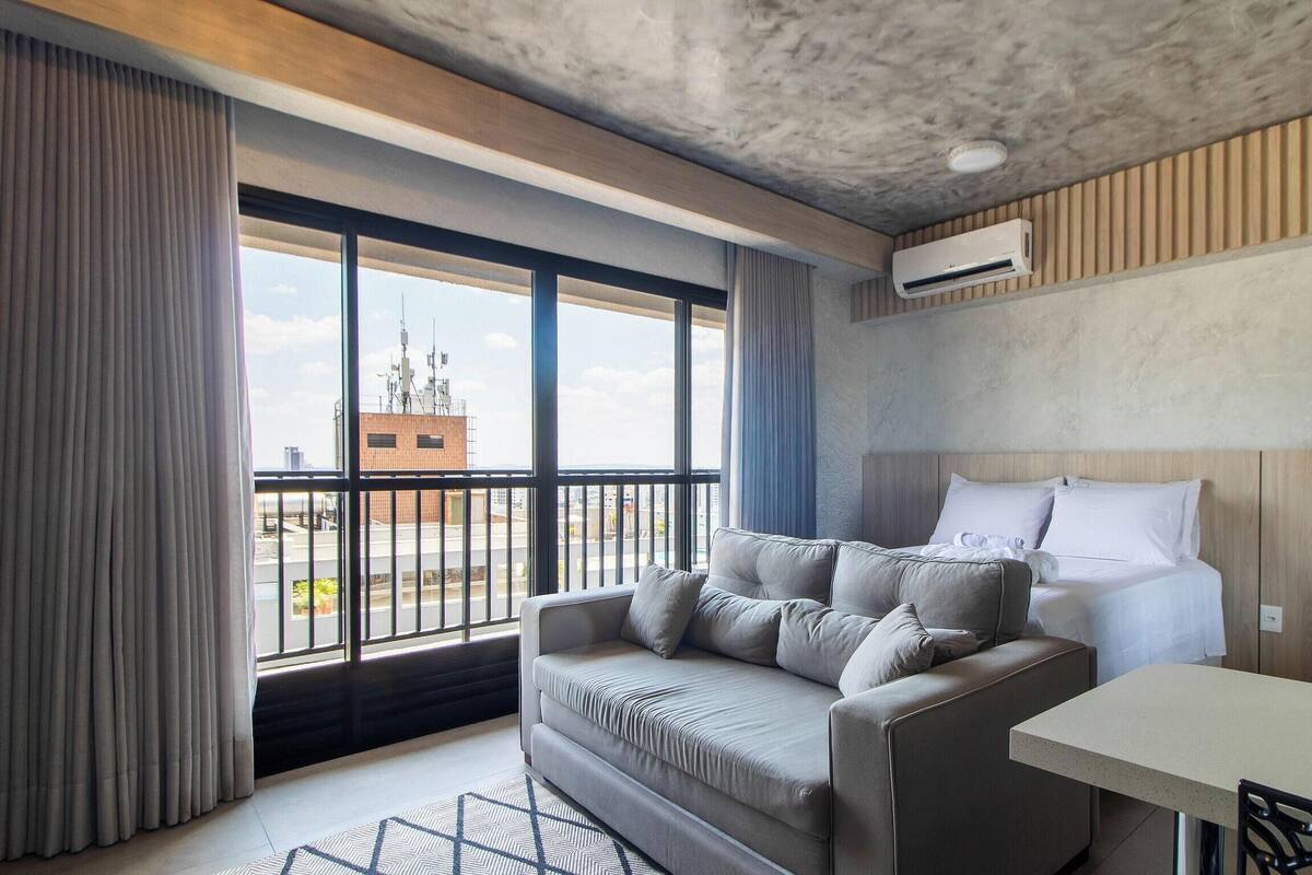 Een hotelkamer met een groot raam, een bank, een bed, een tafel en een airconditioner.