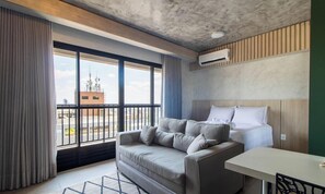 Une chambre d’hôtel avec une grande fenêtre, un canapé, un lit, une table et un appareil de climatisation.