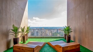 Un balcon avec vue sur la ville, deux bancs en bois et des plantes en pot.