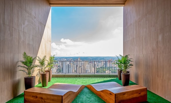 Ein Balkon mit Blick auf eine Stadtlandschaft, zwei Holzliegen und Kübelpflanzen.