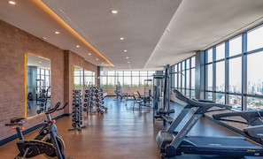 Une salle de sport équipée de matériel d’exercice, dotée de grandes fenêtres et offrant une vue sur la ville.
