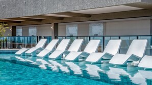 A pool area with white lounge chairs and a modern building in the background. - Lindos apts c piscina no Setor Oeste IDV (Goiânia)