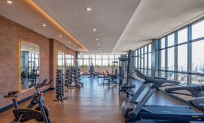 Ein Fitnessstudio mit Trainingsgeräten, großen Fenstern und Blick auf die Stadt.