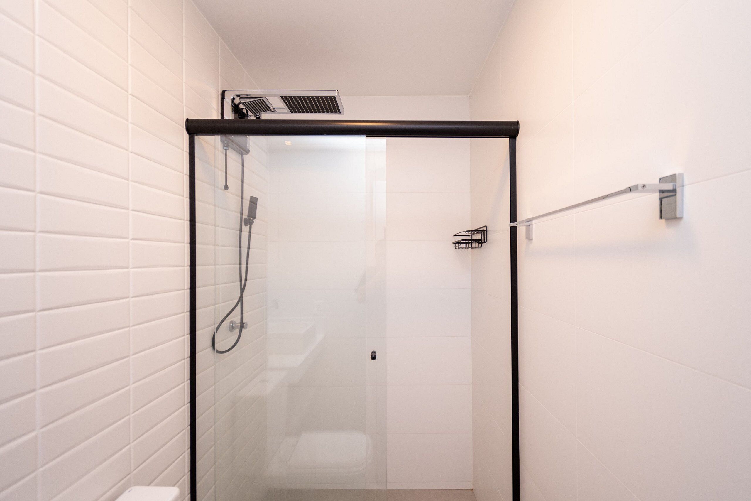 A glass-enclosed shower with a black frame, white tiled walls, and a visible showerhead.