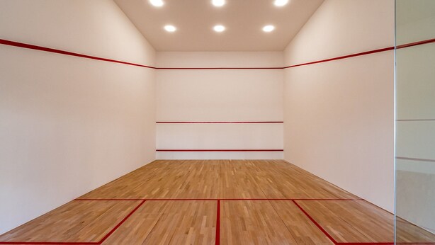 Un court de squash doté d’un plancher en bois et de lignes de démarcation rouges.