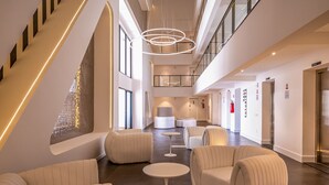 A spacious lobby with a high ceiling, modern furniture, and a central seating area. - Lindos apts c piscina no Setor Oeste IDV (Goiânia)