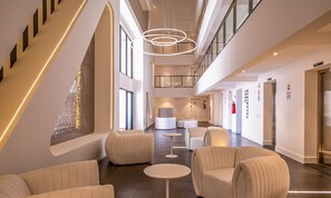 Eine geräumige Lobby mit hoher Decke, modernen Möbeln und einer zentralen Sitzgruppe.