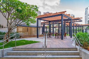 A covered outdoor seating area with steps leading up to it, surrounded by greenery and a building in the background. - Lindos apts c piscina no Setor Oeste IDV (Goiânia)