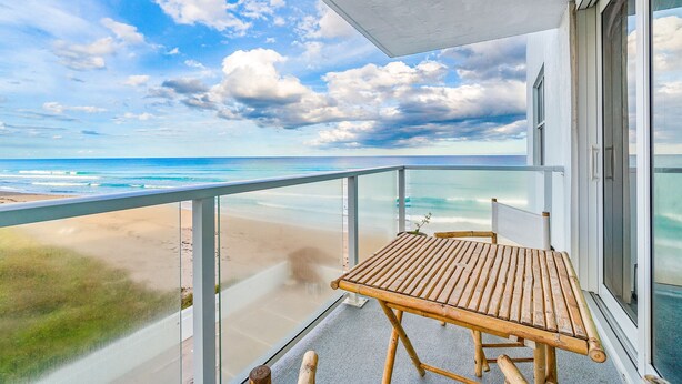 A balcony with a wooden table and chairs, overlooking a beach and ocean. - Palm Beach Island Seasonal Rental 6 month required 
Oceanfront 2 bed 2 bath  (Palm Beach)