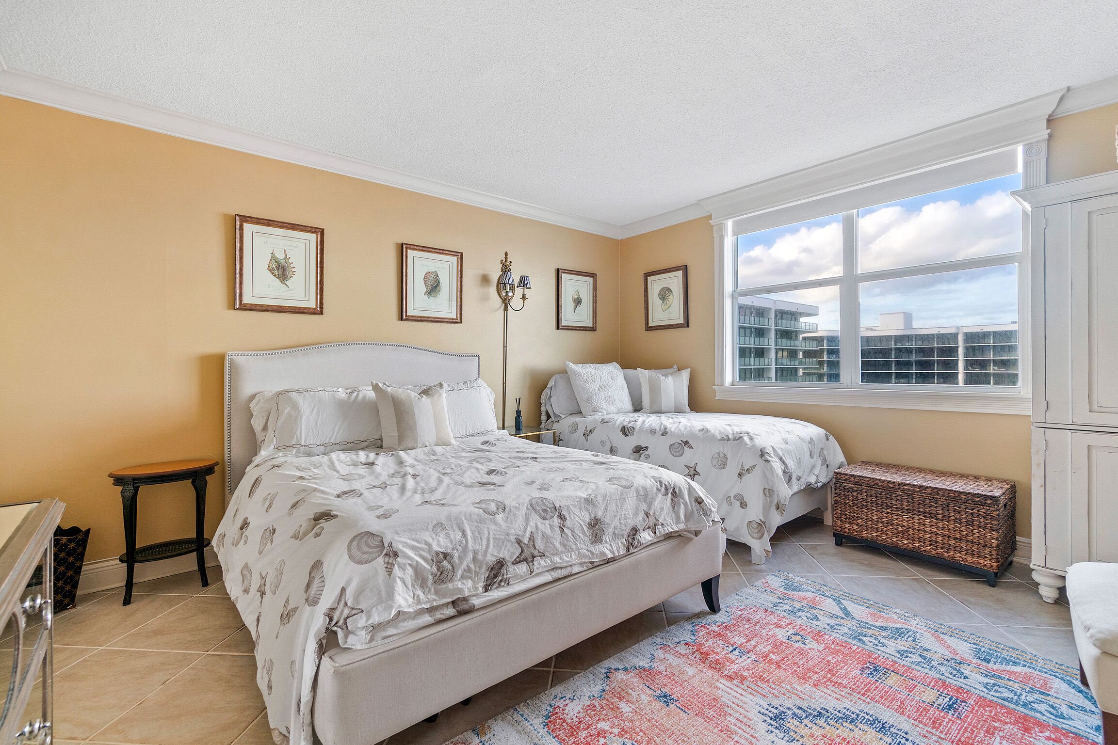 A bedroom with two beds, a large window, and framed artwork on the wall.