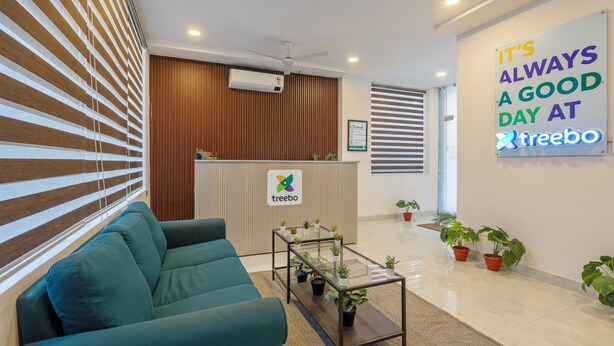 A reception area with a green sofa, a glass-top table with plants, a wooden panel wall, and a sign that reads "It's always a good day at treebo." - Treebo De Alphabet Gachibowli (Hyderabad)