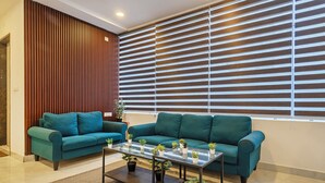 A modern living room with two teal sofas, a glass coffee table, and a wooden accent wall. - Treebo De Alphabet Gachibowli (Hyderabad)