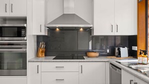 A modern kitchen with stainless steel appliances, a black range hood, and a wooden bowl on the countertop. - Colloden Beach House by Experience Jervis Bay (Vincentia)
