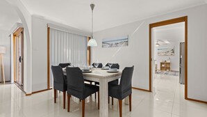 A modern dining room with a white table, black chairs, and a pendant light. - Colloden Beach House by Experience Jervis Bay (Vincentia)