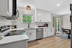 A modern kitchen with white cabinetry, a built-in oven, and a window with a view of greenery. - Hot Tub Retreat. 2 King Beds. Game Room Fun (Saint Charles)