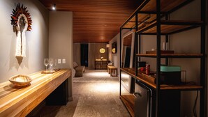 Un pasillo estrecho con un banco de madera a la izquierda, un estante con marco negro a la derecha y un área de comedor al fondo.