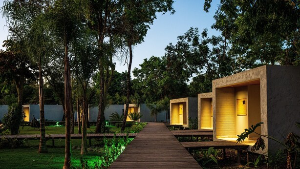 Un sendero de madera que lleva a cabañas modernas y bien iluminadas, rodeadas de exuberante vegetación.