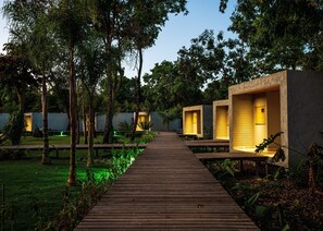 A wooden pathway leading to modern, well-lit cabins surrounded by lush greenery. - Amaná Hotel (Alto Paraíso de Goiás)