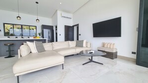 Un salon moderne avec un canapé d’angle, une table basse ronde et un téléviseur fixé au mur.
