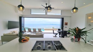 Un salon moderne doté d’une grande fenêtre, d’un coin repas et d’une cuisine équipée d’une cuisinière à gaz.